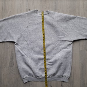 May include: A gray sweatshirt with a yellow measuring tape running down the center back. The sweatshirt is laid flat on a wooden surface.
