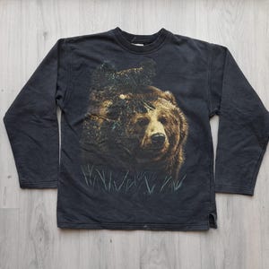 May include: Black long-sleeved sweatshirt with a graphic print of a brown bear in a forest setting.