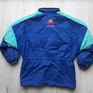 Puede incluir: Chaqueta azul, turquesa y azul marino con cintura con cord&oacute;n. La chaqueta tiene cuello negro y un logotipo en la parte superior de la espalda. La chaqueta est&aacute; hecha de un material ligero.