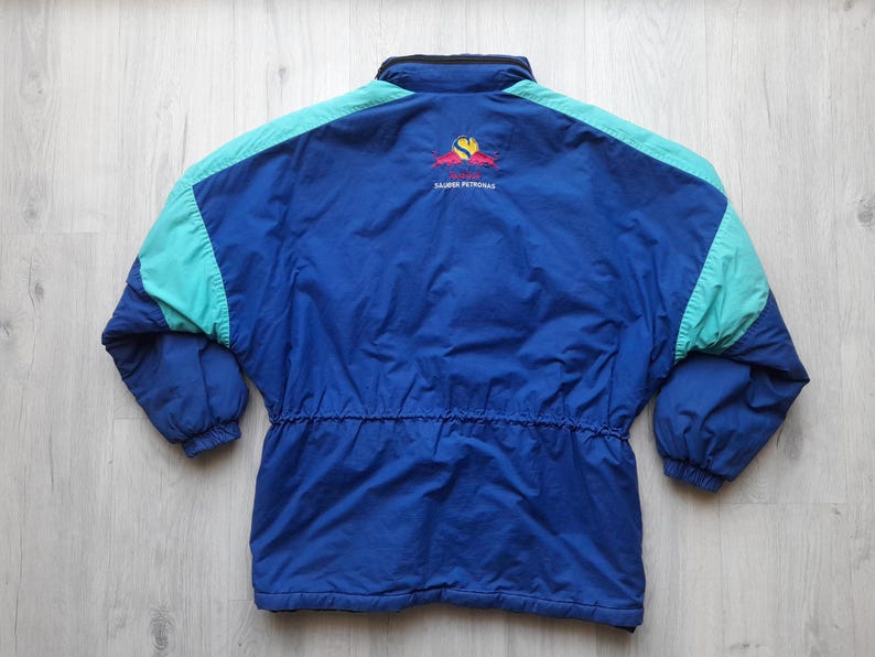 Puede incluir: Chaqueta azul, turquesa y azul marino con cintura con cord&oacute;n. La chaqueta tiene cuello negro y un logotipo en la parte superior de la espalda. La chaqueta est&aacute; hecha de un material ligero.