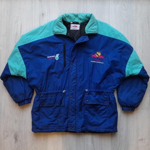Puede incluir: Chaqueta vintage azul, turquesa y negra con el logo de Petronas. La chaqueta tiene cuello y hombros turquesa, dos bolsillos delanteros y una cremallera negra. El texto "RACING PETRONAS" y un logotipo est&aacute;n en el pecho derecho.