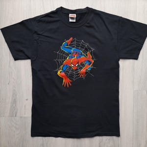 Pu&ograve; includere: T-shirt nera con grafica di Spider-Man. Il supereroe &egrave; raffigurato nel suo costume rosso e blu, appeso a una ragnatela bianca. La maglietta ha un girocollo e maniche corte.