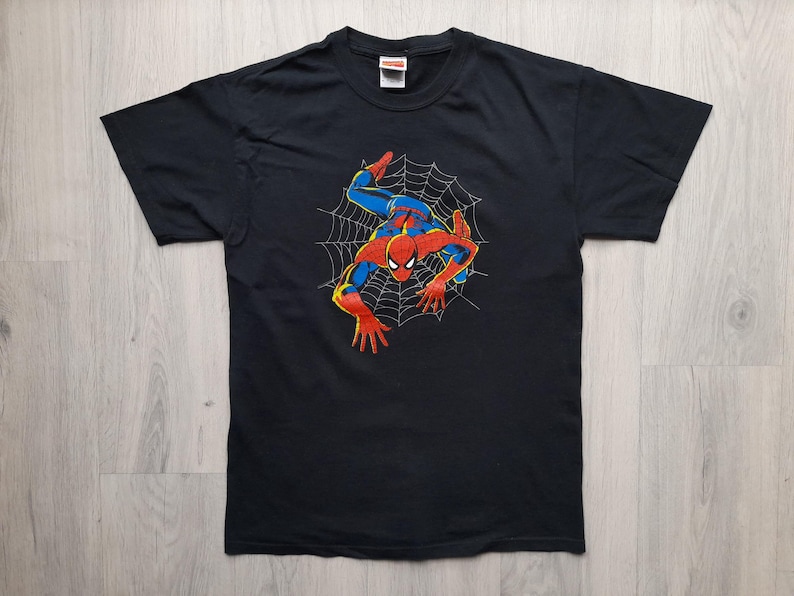 Pu&ograve; includere: T-shirt nera con grafica di Spider-Man. Il supereroe &egrave; raffigurato nel suo costume rosso e blu, appeso a una ragnatela bianca. La maglietta ha un girocollo e maniche corte.