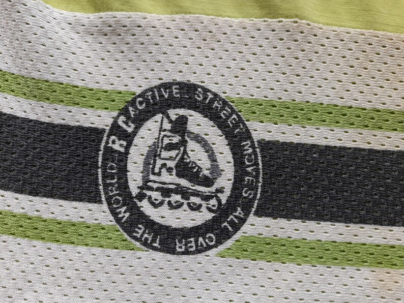 May include: A black and white logo on a green and white striped fabric. The logo says "RC World Active Street Moves All Over The" and features a silhouette of a person rollerblading.