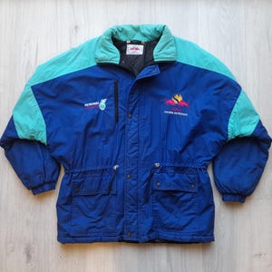 Puede incluir: Chaqueta vintage azul, turquesa y negra con los logotipos de Petronas y Saura Petronas. La chaqueta tiene cremallera, dos bolsillos delanteros y cuello y detalles en los hombros turquesa. Fabricada en material ligero.
