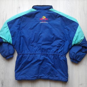 Puede incluir: Chaqueta vintage azul y turquesa con cintura con cord&oacute;n y cuello alto. La chaqueta tiene detalles en los hombros en color turquesa y un logotipo en la espalda. La chaqueta est&aacute; hecha de un material ligero.