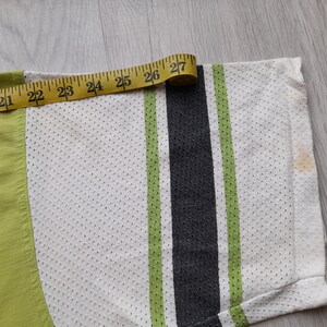 May include: Close-up of a white, green and black striped shirt with a measuring tape showing 27 inches. The shirt is made of a mesh fabric.