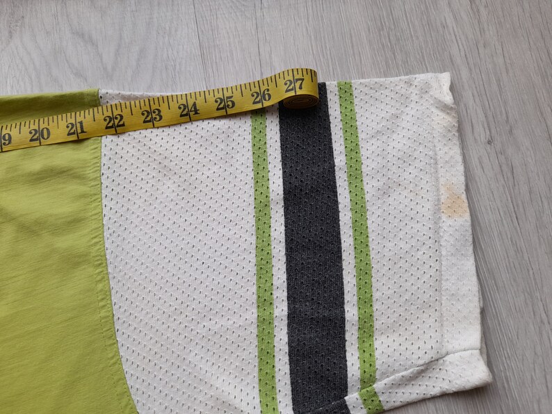May include: Close-up of a white, green and black striped shirt with a measuring tape showing 27 inches. The shirt is made of a mesh fabric.