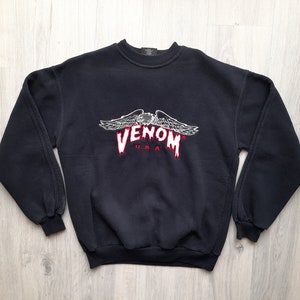 May include: Black sweatshirt with a white embroidered Venom logo with red dripping accents and a winged eagle design. The logo also says "USA" underneath.