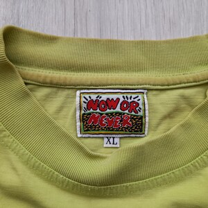 May include: A lime green t-shirt with a yellow and red embroidered patch that says "NOW OR NEVER" and a size tag that says "XL".