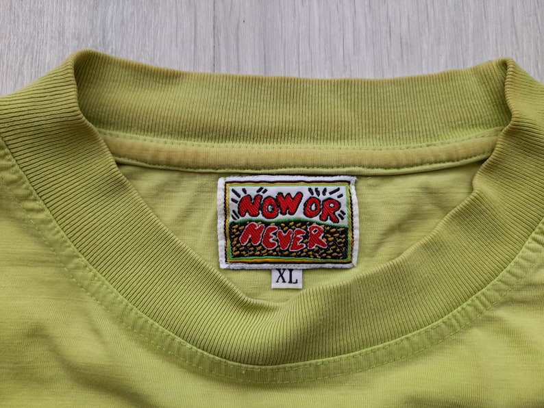 May include: A lime green t-shirt with a yellow and red embroidered patch that says "NOW OR NEVER" and a size tag that says "XL".