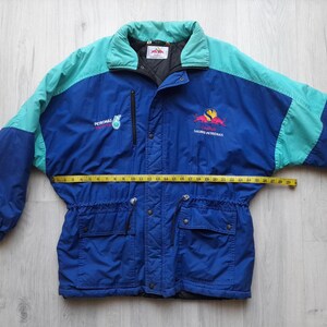 Puede incluir: Chaqueta vintage azul y turquesa con el texto "PETRONAS" y un logotipo. La chaqueta tiene cierre de cremallera, dos bolsillos delanteros y una cinta m&eacute;trica amarilla en la cintura. La chaqueta es talla L.
