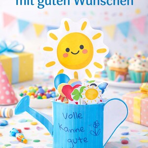 Può includere: Un annaffiatoio blu pieno di decorazioni colorate, tra cui un ritaglio di sole sorridente. Il testo sul vaso recita, "Geschenk für Kinder mit guten Wünschen." Coriandoli e articoli per feste circondano il vaso, suggerendo una celebrazione.
