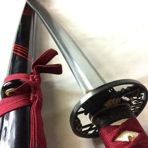 May include: A traditional Japanese katana sword with a black scabbard and red accents. The sword is partially unsheathed, revealing a silver blade and a black and gold metal tsuba (hand guard).