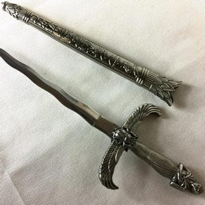 May include: A silver dagger with a decorative handle featuring an Egyptian-inspired design. The blade is sharp and pointed, and the handle is adorned with intricate details. The dagger is a decorative piece and is not intended for use as a weapon.