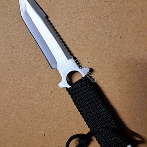 May include: A silver knife with a black paracord handle and a serrated blade. The knife has a lanyard hole and a black cord attached to the handle.