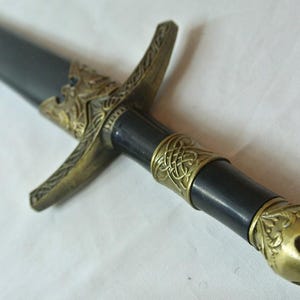 May include: A black and gold dagger with intricate details on the handle and pommel. The blade is sharp and pointed.