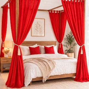 May include: A wooden four-poster bed with bright red curtains. The bed is made with white linens, red pillows, and a beige throw blanket. A beige rug is on the floor. A nightstand with a lamp is on the left.