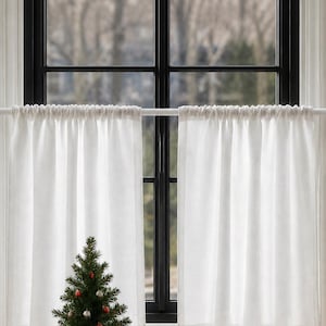 Peut inclure: Un petit sapin de Noël dans un pot en terre cuite est placé devant une fenêtre avec des rideaux blancs. L'arbre est orné de boules rouges et argentées. Une théière décorative et un bol en verre sont également sur le rebord de la fenêtre.