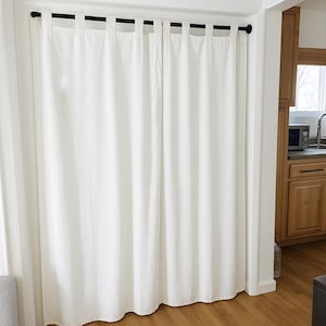Puede incluir: Cortinas de lino color crema colgadas de una barra negra. Las cortinas están hechas de una tela texturizada y tienen un diseño simple y elegante. Las cortinas cuelgan en una puerta, con un suelo de madera.