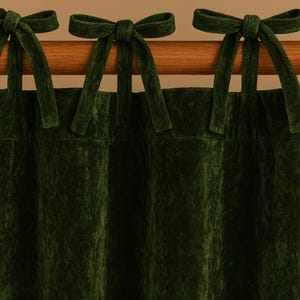 May include: Dark green velvet curtains with matching tie-up bows. The curtains are hanging from a wooden rod, creating a luxurious and elegant look. The fabric has a soft, textured appearance.