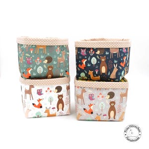 Könnte beinhalten: Vier quadratische Stoffaufbewahrungskörbe mit einem Waldtierdruck. Die Körbe sind übereinander gestapelt. Der Druck zeigt Hirsche, Eulen, Füchse, Bären und Igel in Braun-, Grün-, Blau- und Orangetönen.