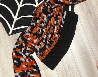 May include: A black, orange, white, and purple crocheted sweater with long sleeves. The sweater has a geometric pattern.