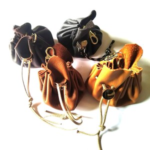 Può includere: Quattro piccoli sacchetti in pelle con coulisse nei colori nero, marrone scuro, cuoio e marrone chiaro. Ogni sacchetto presenta un fermacorda in metallo dorato, un moschettone abbinato e un cordino sottile per chiudere l'apertura della borsa.