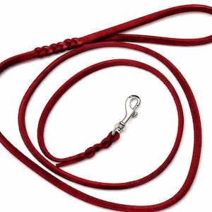 Könnte beinhalten: Eine rote Hundeleine aus Leder mit geflochtenem Griff und einem silberfarbenen Metallverschluss. Die Leine hat einen tiefen, satten Rotton und scheint aus hochwertigem Leder gefertigt zu sein. Für Tierbesitzer.