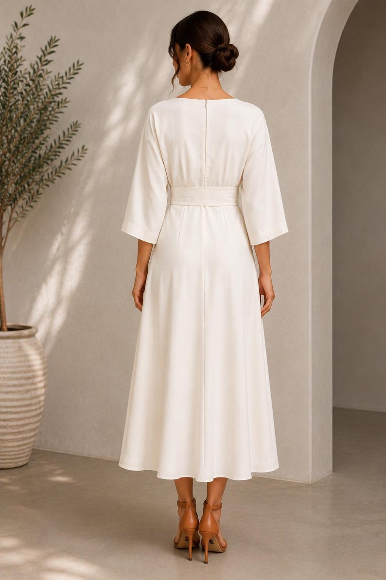 May include: A cream-colored midi dress featuring three-quarter length sleeves, a wide waistband, and a back zipper closure. The garment has a structured bodice and a flowing skirt that falls below the knees, paired with tan high-heeled sandals.