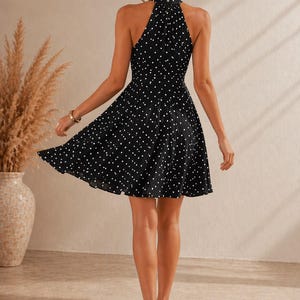 K&ouml;nnte beinhalten: Schwarzes Kleid mit wei&szlig;en Polka Dots, mit Neckholder-Ausschnitt und ausgestelltem Rock. Das Kleid reicht bis zum Knie. Die Person tr&auml;gt nudefarbene Abs&auml;tze. Ein stilvolles und vielseitiges Kleidungsst&uuml;ck.
