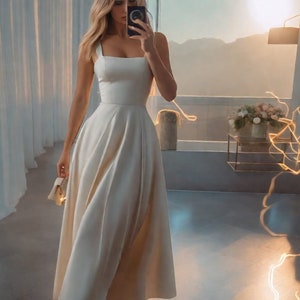 May include: A white sleeveless dress with a square neckline and a flowing skirt. The dress is made of a smooth, silky fabric.