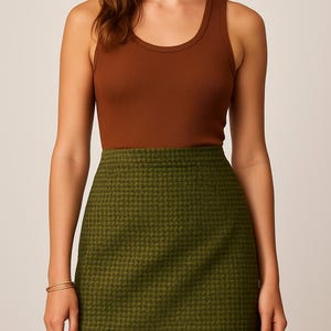K&ouml;nnte beinhalten: Outfit einer Frau mit einem braunen, gerippten Tanktop und einem gr&uuml;nen, strukturierten Minirock. Der Rock hat ein kleines, sich wiederholendes Muster. Ein goldenes Armband ist am linken Handgelenk zu sehen. Das Outfit ist f&uuml;r den Freizeitgebrauch geeignet.