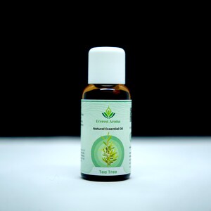 Puede incluir: Una pequeña botella de vidrio marrón con una tapa blanca, etiquetada "Everest Aroma Aceite Esencial Natural Tea Tree". La etiqueta tiene un logotipo verde con un árbol estilizado y una persona meditando.