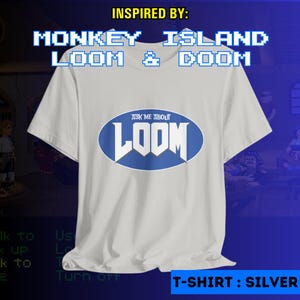 Może przedstawiać: Srebrny t-shirt z niebiesko-białym owalnym wzorem z napisem "ASK ME ABOUT LOOM". Koszulka zawiera również tekst "INSPIRED BY: MONKEY ISLAND LOOM & DOOM" i "T-SHIRT: SILVER".