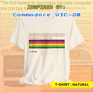 May include: A white t-shirt with a retro-style graphic of the Commodore VIC-20 computer. The graphic features a rainbow color scheme and the text "Commodore VIC-20: 1980". The t-shirt is labeled "T-SHIRT: NATURAL".