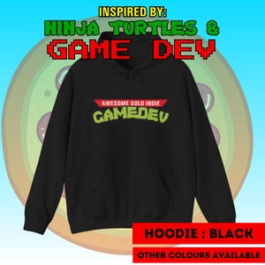 Peut inclure: Un sweat à capuche noir avec le texte "AWESOME SOLO INDIE GAMEDEV" en vert et rouge. Le sweat à capuche porte également le texte "INSPIRED BY: NINJA TURTLES & GAME DEV". Le bas de l'image indique "HOODIE: BLACK" et "OTHER COLOURS AVAILABLE".
