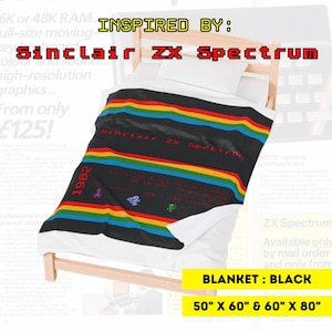 Może przedstawiać: Czarny koc z tęczowym wzorem w paski, inspirowany Sinclair ZX Spectrum. Koc zawiera tekst "Sinclair ZX Spectrum" i "1982". Dostępny w rozmiarach 127cm x 152cm i 152cm x 203cm.