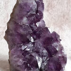 May include: A large amethyst crystal cluster with a deep purple colour. The crystal has many points and facets, and it is a beautiful example of this popular gemstone.