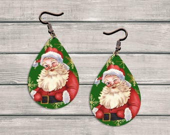 May include: A pair of teardrop-shaped earrings featuring a vintage Santa Claus design. The earrings have a green background with gold snowflakes. Santa is wearing a red suit and hat, with a white beard and is winking. The earrings have bronze-colored ear wires.