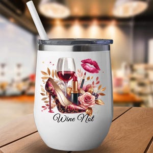 May include: White insulated wine tumbler with a silver lid and a white straw. The tumbler features a design with a high-heeled shoe, a glass of red wine, lipstick, and the words "Wine Not."