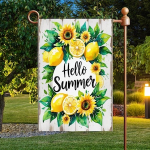 May include: A garden flag with a watercolor design featuring lemons, sunflowers, and green leaves. The words "Hello Summer" are in a white circle. The flag is displayed on a brown metal stand in a garden setting.
