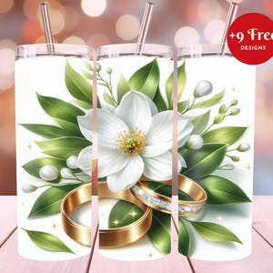 Puede incluir: Vaso blanco con un diseño floral, que incluye una gran flor blanca, hojas verdes y anillos de boda dorados. El diseño incluye una pajita dorada y el texto "+9 Free Designs" en un círculo rojo.