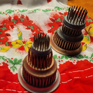 May include: Close-up of three vintage flower frogs with metal pin holders. The frogs are various sizes and colors, including copper, bronze, and green. They sit on a red and white floral tablecloth with a Christmas theme.