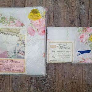 May include: Two packages of French Bouquet Perma-Prest percale bed linens in white with a pink rose floral pattern. Each package features a gold Neatniks label and a product information card detailing the 50% cotton and 50% polyester blend.