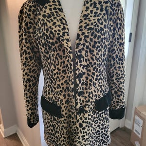 May include: A leopard print blazer with black velvet collar, pocket trim, and cuffs. The jacket has a classic tailored design with a button closure. The animal print features black spots on a tan background.