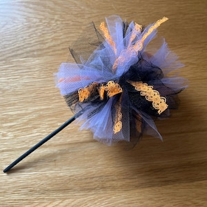May include: A Halloween wand featuring a black handle and a decorative top. The top is made of layered black, white, and orange tulle, with orange lace detailing. The wand is designed for festive occasions.