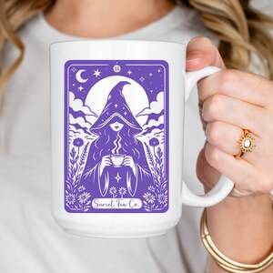 Tarot card design graphic with a mysterious woman wearing a hooded cloak and drinking tea, surrounded by wildflowers, stars and large moon in the sky. Text Suriel Tea Co at the bottom. ACOTAR inspired PNG SVG DXT cut file. Perfect for print on demand
