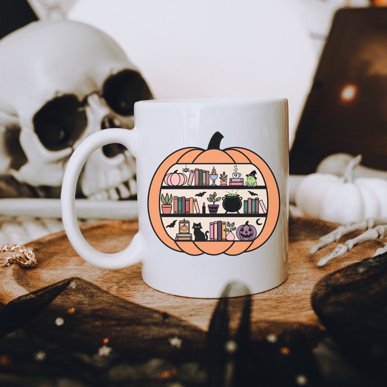 May include: White ceramic mug with a black outline of a pumpkin. The pumpkin is filled with books, a cauldron, a cat, and other Halloween-themed items.