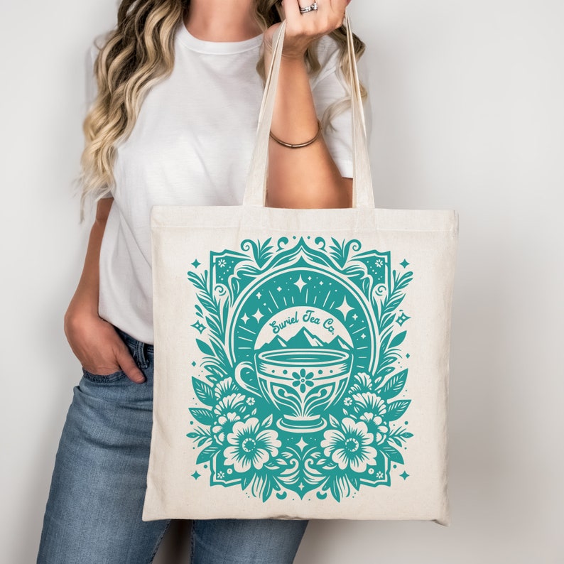 A decorative tarot card design featuring a teacup against a backdrop of mountains and stars, adorned with floral elements. The text reads Suriel Tea Co. ACOTAR inspired graphic. PNG, JPG, DXF Cut File, and SVG. Works in Canva. Gift for fantasy reader